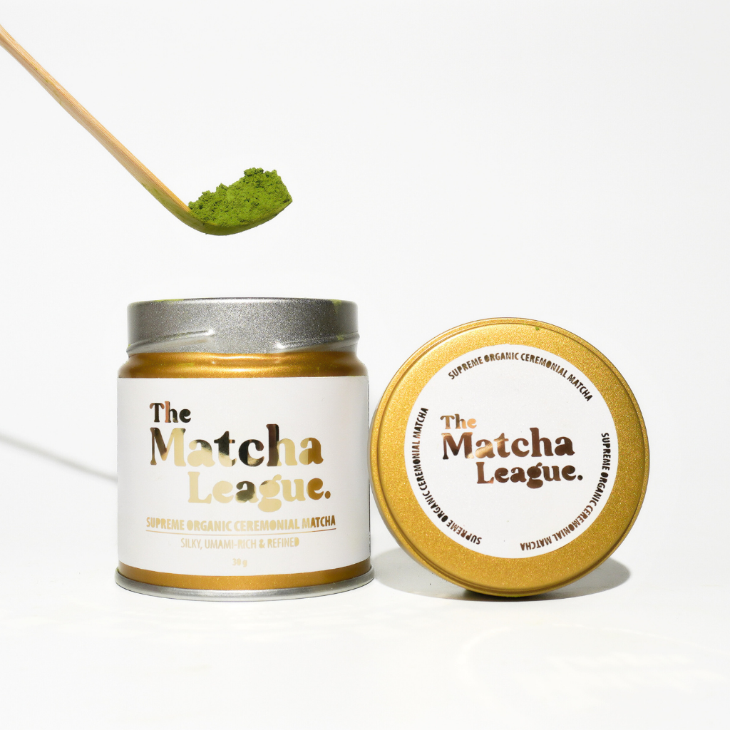 The Matcha League Supreme organic ceremonial matcha in goudkleurig potje met felgroene matcha op bamboe lepel